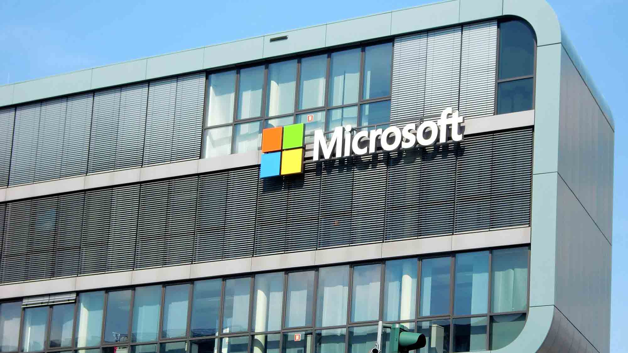Ein modernes Bürogebäude mit großen Fenstern und dem Microsoft-Logo auf der Fassade, mit dem Firmennamen und dem vierfarbigen quadratischen Symbol. Das Gebäude steht unter einem klaren blauen Himmel.