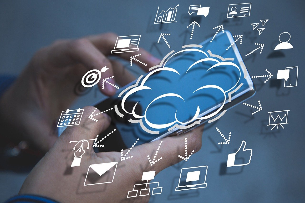 Hände, die ein Smartphone mit einem Wolkensymbol und verschiedenen herumschwebenden digitalen Symbolen halten, die Cloud Computing und internetbasierte Dienste wie E-Mail, soziale Medien, Datenanalyse und Online-Kommunikation darstellen.